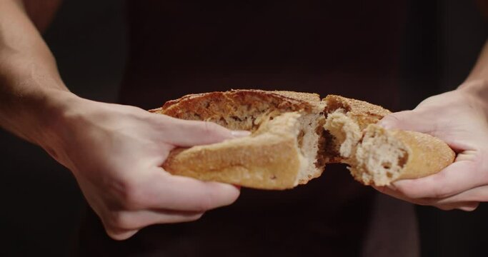 A man tears a loaf of freshly baked bread in half. 