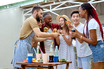 Side View Portrait Of International People Gathered Together On Terrace Eating Burgers, Young People In Casual Outfit Enjoy Spending Summer Holidays Outdoors, Talking, Communicating. People Lifestyle