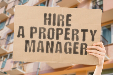 The phrase " Hire a property manager " on a banner in men's hand with blurred background. Collaboration. investor. Lawyer. Realty. Sell. Selling. Dealing. Condominium. Real estate agent. Renting