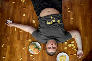 Top view on glutton teen boy surrounded by junk food, overeating concept. Overweight kid in casual...
