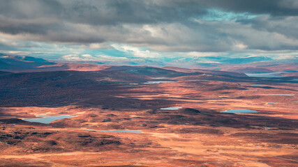Landscape of Pieljekaise National Park in autumn with lakes and snowy mountains in Lapland in Sweden, colored plants, dramatic light and clouds in sky.
