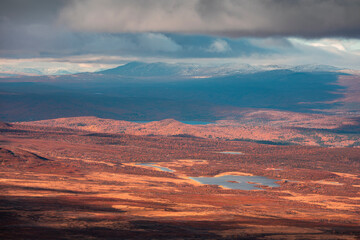 Landscape of Pieljekaise National Park in autumn with lakes and snowy mountains in Lapland in Sweden, colored plants, dramatic light and clouds in sky.