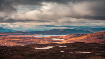 Landscape of Pieljekaise National Park in autumn with lakes and snowy mountains in Lapland in Sweden, colored plants, dramatic light and clouds in sky.