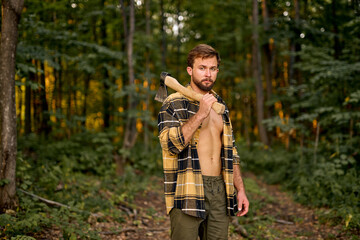 Lumberman work with ax in summer forest. Strong lumberjack in plaid shirt. Stylish handsome caucasian lumberman getting ready for work. Lifestyle. Hard work in forest. Illegal logging. Portrait