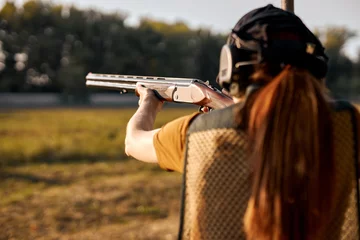 Fototapeten Rear view redhead caucasian woman on tactical gun training classes. Woman with weapon. Outdoor Shooting Range. Side view on beautiful lady with rifle machine gun in the forest, slim female is hunting © Roman