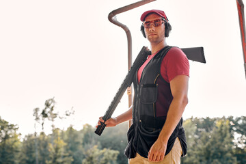 Handsome Caucasian Guy In Protective Goggles, Headset And Cap Posing With Rifle, Have Rest After...