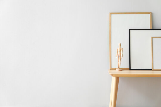 Wooden bench with blank frames and mannequin near light wall