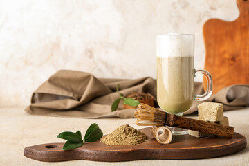 Wooden board with glass of hojicha latte, chasen, powder and marshmallows on light background