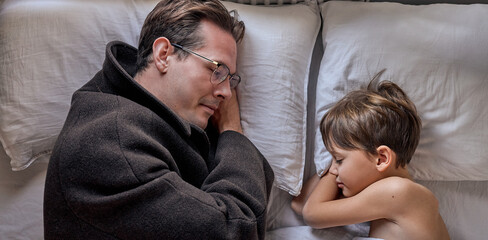 Sad caucasian dad lying with little son before leaving for long business trip, upset father came to...