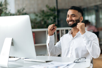 Happy successful young adult Indian business leader, manager or office worker with beard sitting in...