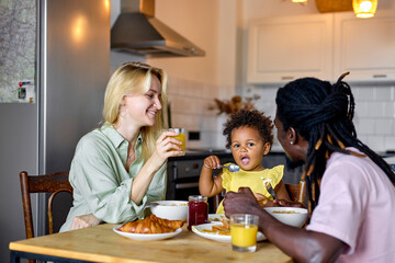 Young Family with child having breakfast at home. Happy lifestyle family moments. place where family unites. Loving diverse parents taking care of their little child at home. in the morning