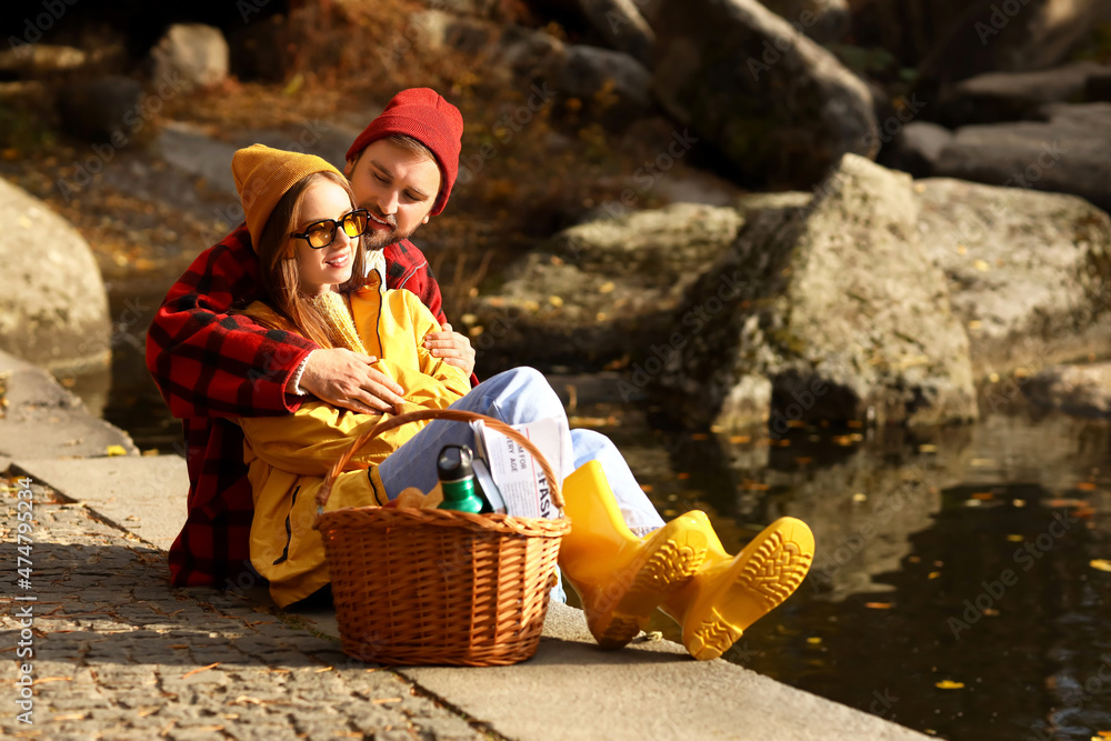 Poster Young loving couple sitting near pond in autumn park