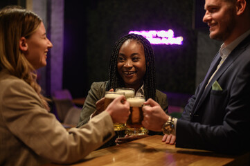 Cheerful colleagues drinking beer in the bar together after work and using a tablet