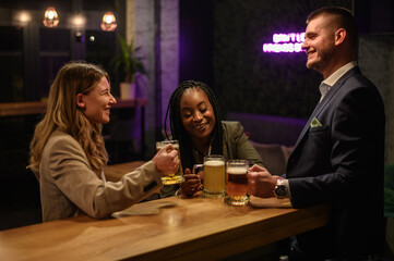 Cheerful colleagues drinking beer in the bar together after work and using a tablet