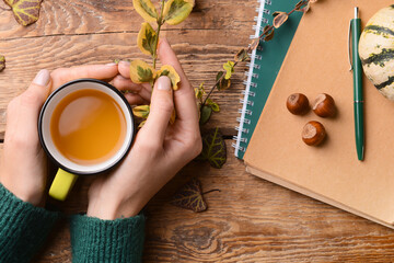 Female hands with cup of tea, notebooks and pen on wooden background, closeup