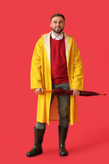 Young man in stylish raincoat and with umbrella on color background