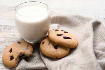 Tasty homemade cookies with chocolate chips and glass of milk on light wooden background, closeup