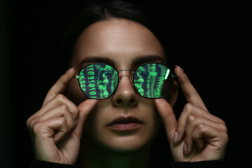 Woman with reflection of matrix code in her tinted glasses on dark background