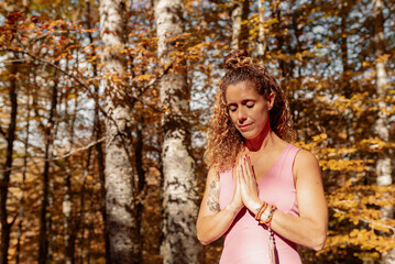 Latin woman with her hands together and eyes closed meditating in the forest during fall.
