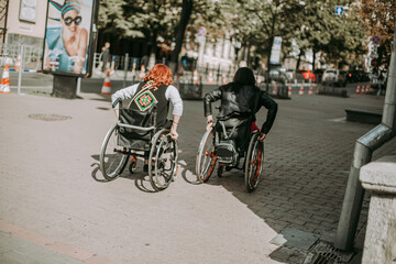 Two girls in wheelchairs near an advertising banner with a smiling girl. Women with special need walk around Kiev near Khreshchatyk and admire the sights. Happy girl on a wheelchair with her friend