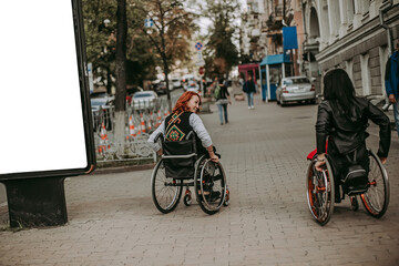 Two girls in wheelchairs near an advertising banner with a smiling girl. Women with special need walk around Kiev near Khreshchatyk and admire the sights. Happy girl on a wheelchair with her friend