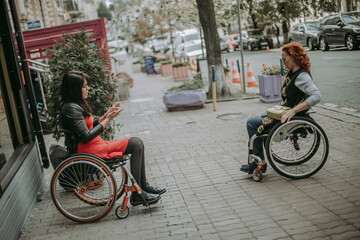Obraz premium Two girls in wheelchairs travel through the central streets. Friends with special needs communicate on the streets of the city