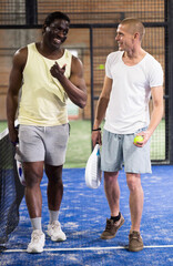 Two men with rackets in their hands chatting after playing padel on the tennis court