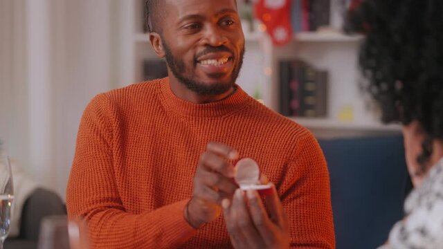 Young black man surprising girlfriend with proposal at Christmas dinner table