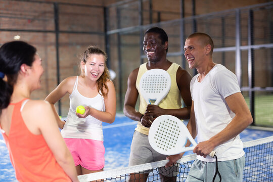 Four smiling sportsmens men and women with padel rackets posing at court inside