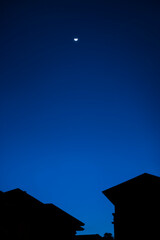 Night sky with view of dark buildings and moon 