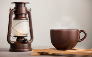 brown cup of coffee with hot steam, on desk with sunlight lamp, white grey background