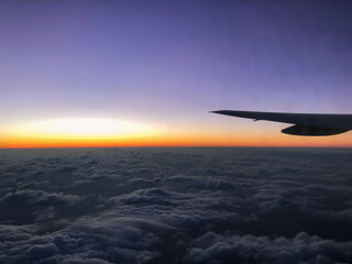 飛行機の窓からみた雲の上から見える朝焼け