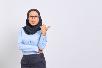 Portrait of shocked young Asian woman pointing thumbs at copy space isolated on white background