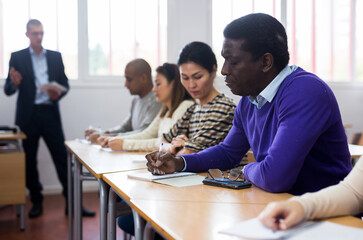 African american adult man attentively listening and making notes of lecture in classroom with...