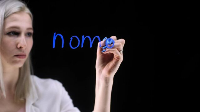 The girl writes a blue marker on a word on a black background. Nomophobia on the transparent board.