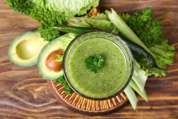 Glass of healthy green smoothie and vegetables on wooden background