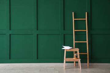 Wooden step stool with book and ladder near green wall