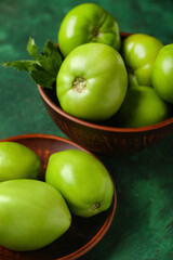 Bowls with green tomatoes on color background, closeup