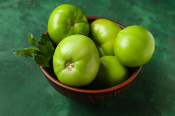 Bowl of green tomatoes on color background