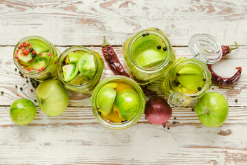 Jars with canned green tomatoes on white wooden background