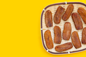 Sun dried bananas in bamboo basket on yellow background.
