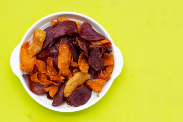 Purple and yellow sweet potato chips in bowl on green background.