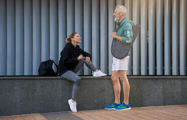Middle aged sportspeople, man and woman in sportswear having a conversation outdoors while waiting...