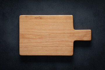 Handmade cherry wood cutting board on the dark tabletop.