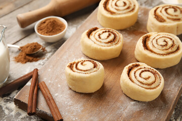 Board with uncooked cinnamon rolls on wooden background, closeup