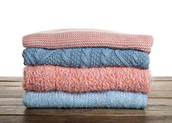 Stack of trendy warm sweaters on wooden table against white background