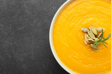 Bowl of tasty pumpkin cream soup on black background, closeup
