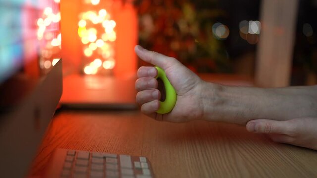 Closeup of man holding green expander in arm at home, take a break from working on computer, does exercise to prevent carpal tunnel syndrome. Male gripping hand expander. Wrist disease concept
