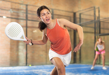 Young asian woman in orange t-shirt playing padel tennis indoor - obrazy, fototapety, plakaty