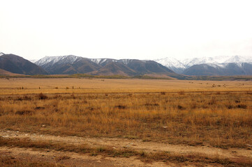 Fototapeta na wymiar Deserted and dry steppe at the foot of a mountain range with snow-capped peaks in early autumn.